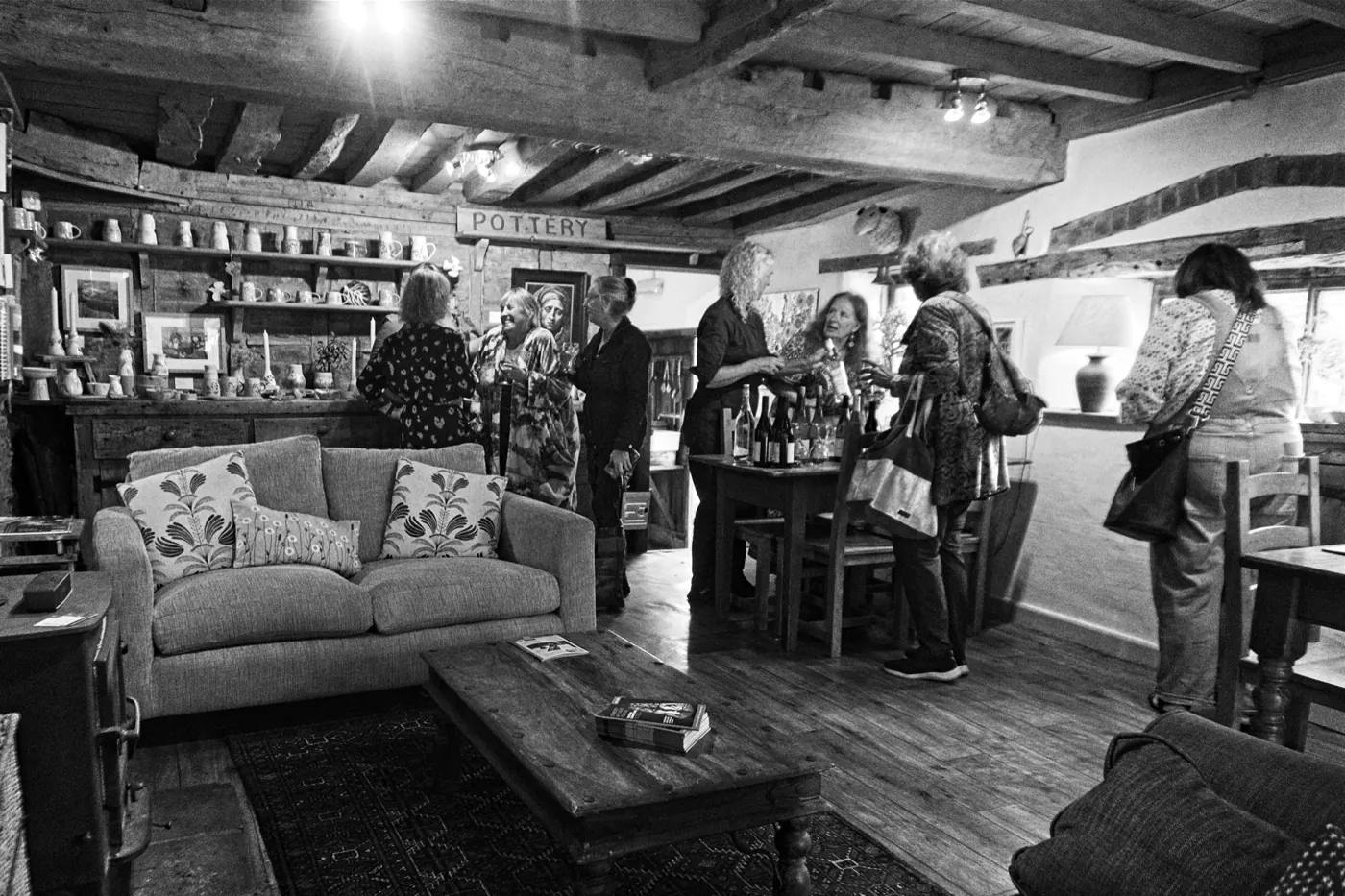 Black and white photo of visitors in a beamed gallery with sofas