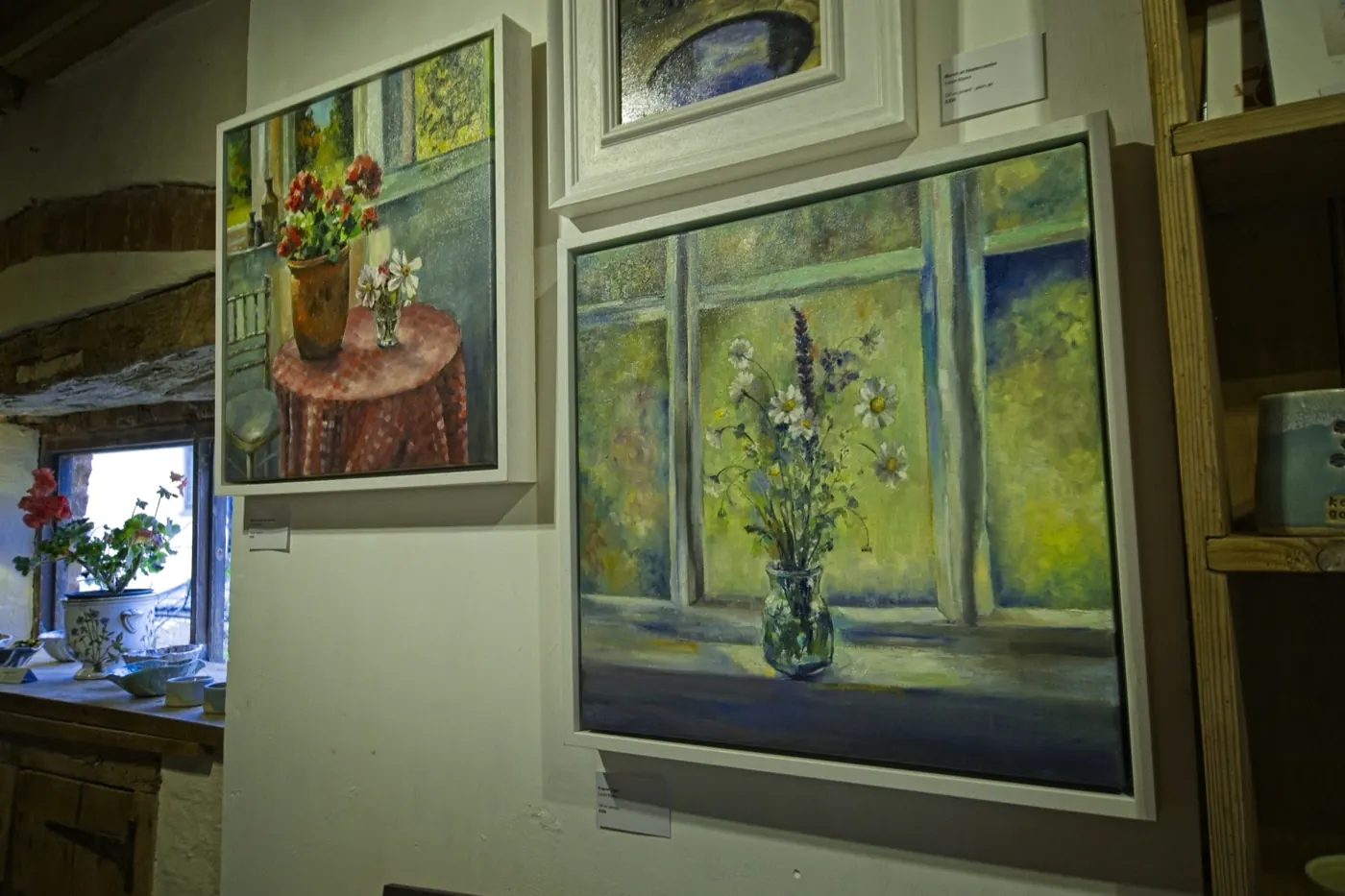 Still life paintings of wildflowers and geraniums in a beamed gallery