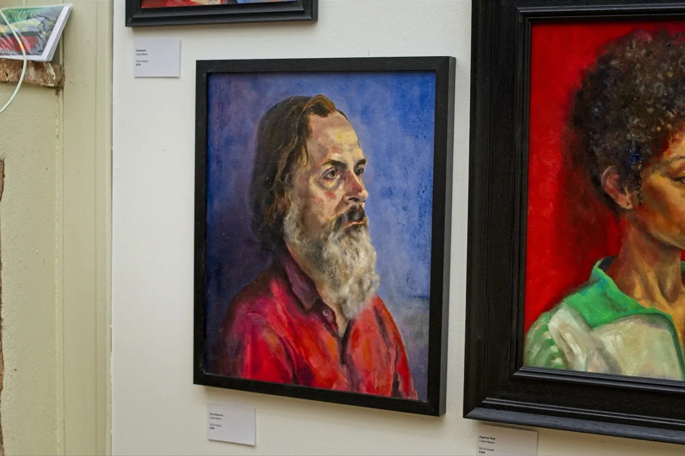Portrait of a bearded man in a red shirt beside a portrait on a red ground